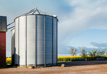 Steel grain bin at farm with cornfield and rural landscape in background