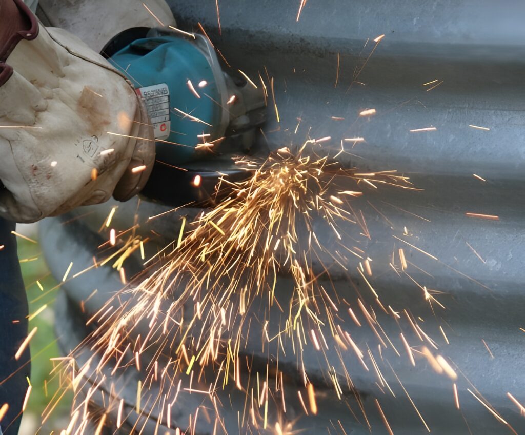 Worker using grinder to repair metal grain bin with sparks flying.