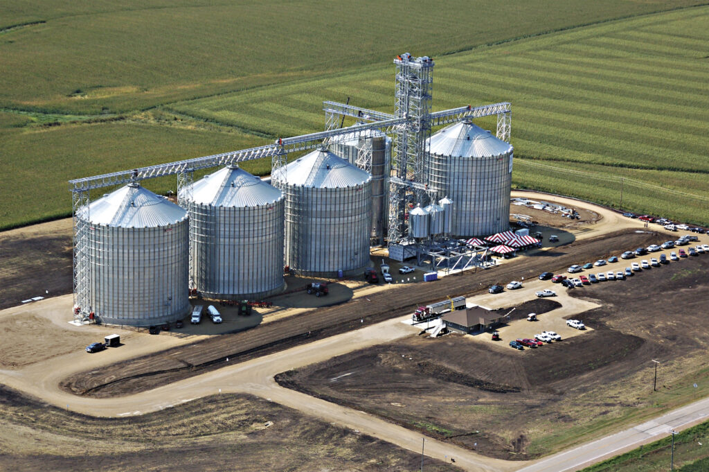 Commercial grain storage facility with steel grain bins, elevator system, and surrounding agricultural fields.